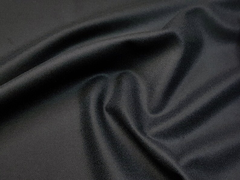 Puede incluir: Un primer plano de una tela negra con una textura suave y lisa. La tela est&aacute; drapeada y doblada, creando una sensaci&oacute;n de profundidad y dimensi&oacute;n.