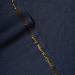 Op de afbeelding: Een close-up van een donkerblauwe stofstaal met een gouden label waarop "VIFALE BARBERIS CANONICO" en "IN ITALY" staat.
