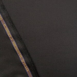 Puede incluir: Primer plano de una tela negra con una etiqueta marr&oacute;n oscuro y dorada que dice "Ermenegildo Zegna" y "CANONICO 1593".
