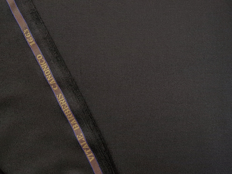 Puede incluir: Primer plano de una tela negra con una etiqueta marr&oacute;n oscuro y dorada que dice "Ermenegildo Zegna" y "CANONICO 1593".