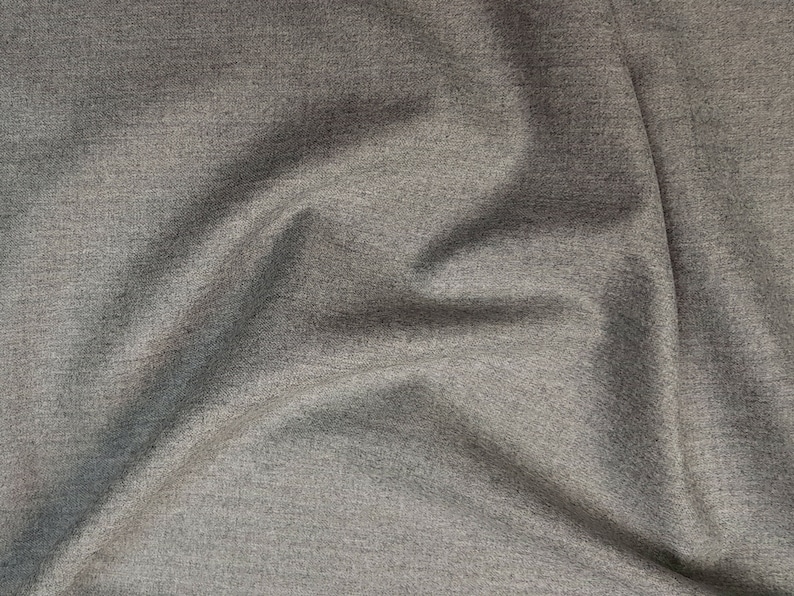 May include: Close-up of a gray, textured fabric with a subtle sheen. The fabric is wrinkled and folded, creating a soft, draping effect.