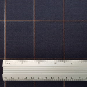K&ouml;nnte beinhalten: Nahaufnahme eines dunkelblauen Stoffes mit einem dezenten orange-wei&szlig;en Karomuster. Ein Lineal liegt auf dem Stoff und zeigt die Skala in Zoll.