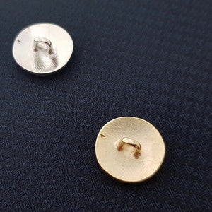 May include: Two round buttons, one silver and one gold, with a loop on the back for sewing.