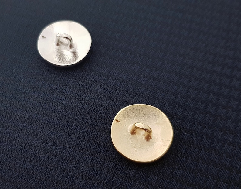 May include: Two round buttons, one silver and one gold, with a loop on the back for sewing.