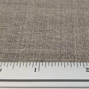 May include: Close-up of a beige fabric with a woven texture. A ruler is placed at the bottom of the image, showing measurements in inches.