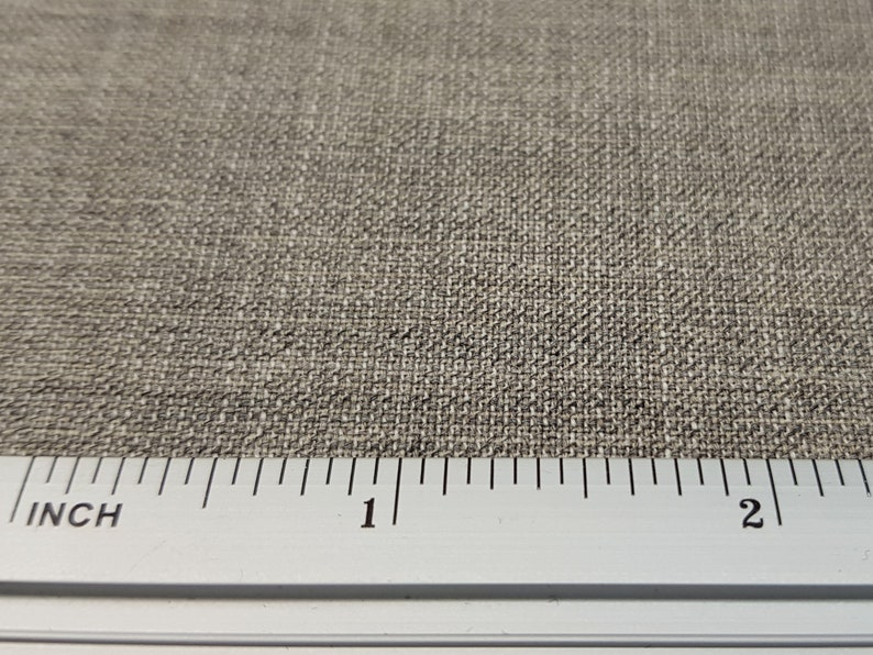 May include: Close-up of a beige fabric with a woven texture. A ruler is placed at the bottom of the image, showing measurements in inches.