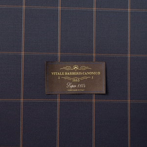 K&ouml;nnte beinhalten: Ein braunes Stoffmuster mit einem goldenen Etikett, auf dem "VITALE BARBERIS CANONICO" mit der Nummer "563" und dem Text "Super 110's" in goldenen Buchstaben steht.