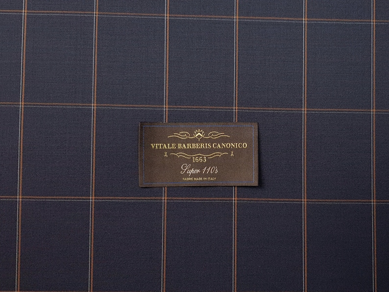 K&ouml;nnte beinhalten: Ein braunes Stoffmuster mit einem goldenen Etikett, auf dem "VITALE BARBERIS CANONICO" mit der Nummer "563" und dem Text "Super 110's" in goldenen Buchstaben steht.