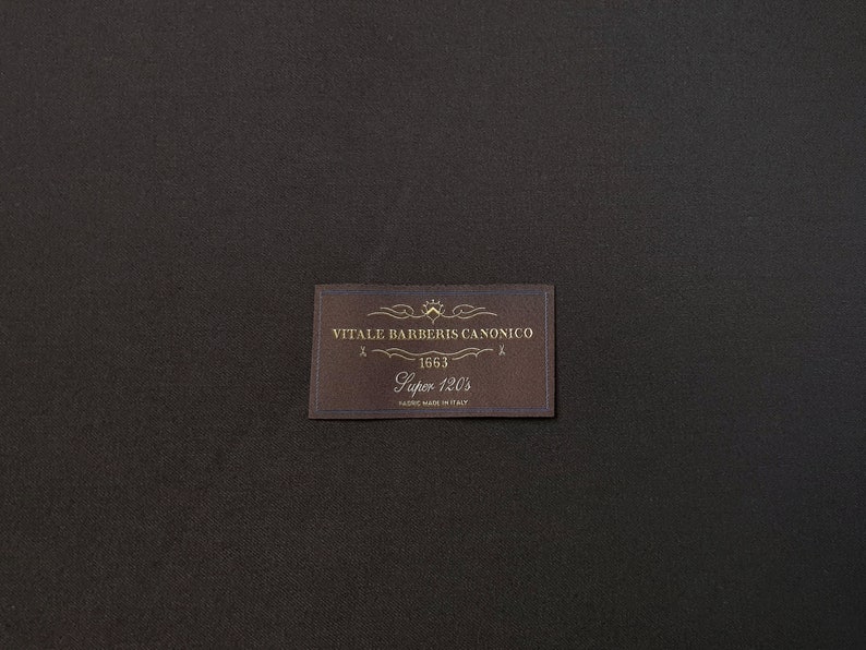 Puede incluir: Una etiqueta marr&oacute;n con texto dorado que dice "VITALE BARBERIS CANONICO 1663 Super 120's FABRIC MADE IN ITALY".