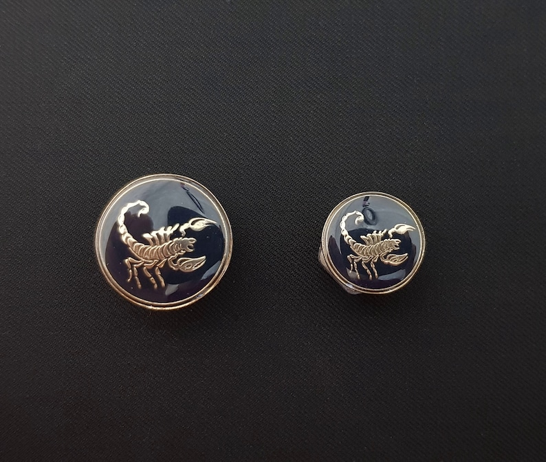 May include: Two round, blue, metal buttons with gold scorpions on them. The larger button is about 1 inch in diameter and the smaller button is about 1/2 inch in diameter.