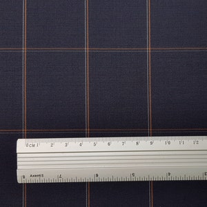 K&ouml;nnte beinhalten: Nahaufnahme eines dunkelblauen Stoffes mit einem wei&szlig;en und orangefarbenen Karomuster. Ein Lineal liegt auf dem Stoff und zeigt die Ma&szlig;e in Zentimetern.