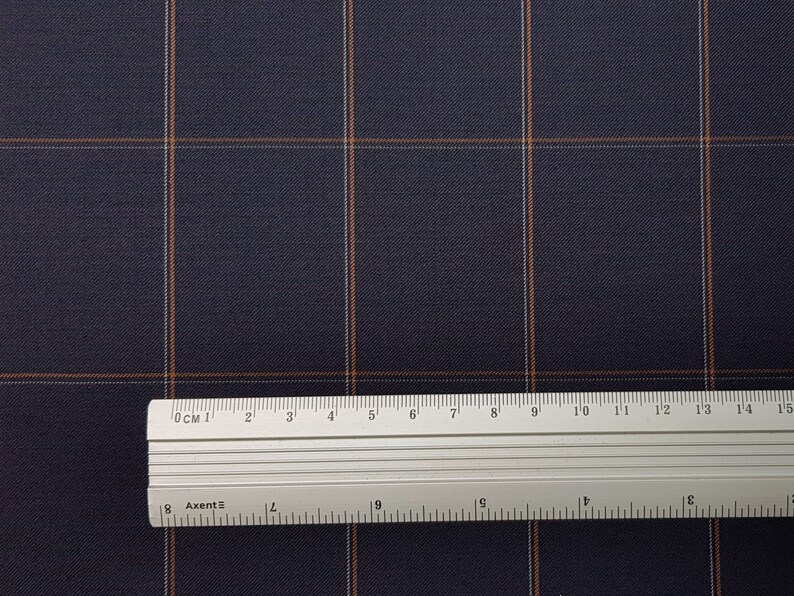 K&ouml;nnte beinhalten: Nahaufnahme eines dunkelblauen Stoffes mit einem wei&szlig;en und orangefarbenen Karomuster. Ein Lineal liegt auf dem Stoff und zeigt die Ma&szlig;e in Zentimetern.