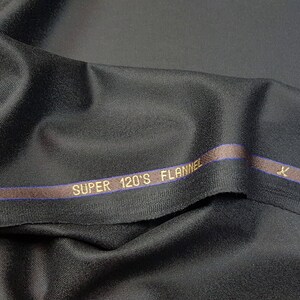 Puede incluir: Tela negra con una franja marr&oacute;n y azul y el texto "SUPER 120'S FLANNEL" en letras doradas.
