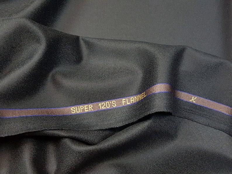 Puede incluir: Tela negra con una franja marr&oacute;n y azul y el texto "SUPER 120'S FLANNEL" en letras doradas.