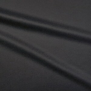 Puede incluir: Primer plano de una tela negra con una superficie lisa y ligeramente texturizada. La tela est&aacute; drapeada y doblada, creando l&iacute;neas suaves y fluidas.