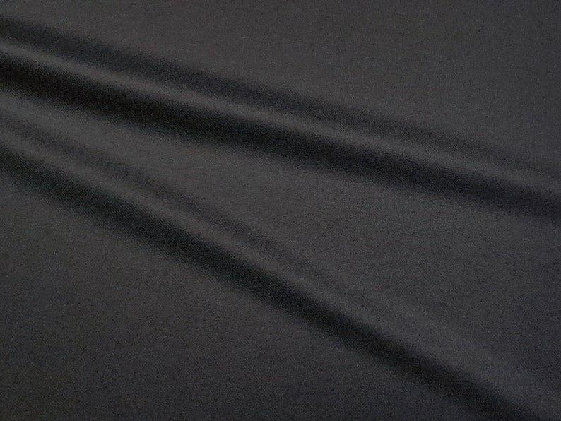 Puede incluir: Primer plano de una tela negra con una superficie lisa y ligeramente texturizada. La tela est&aacute; drapeada y doblada, creando l&iacute;neas suaves y fluidas.
