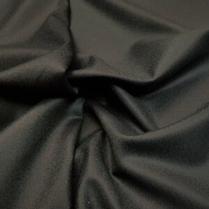 Puede incluir: Primer plano de una tela negra con una textura suave y lisa. La tela est&aacute; drapeada y doblada, mostrando su flexibilidad.