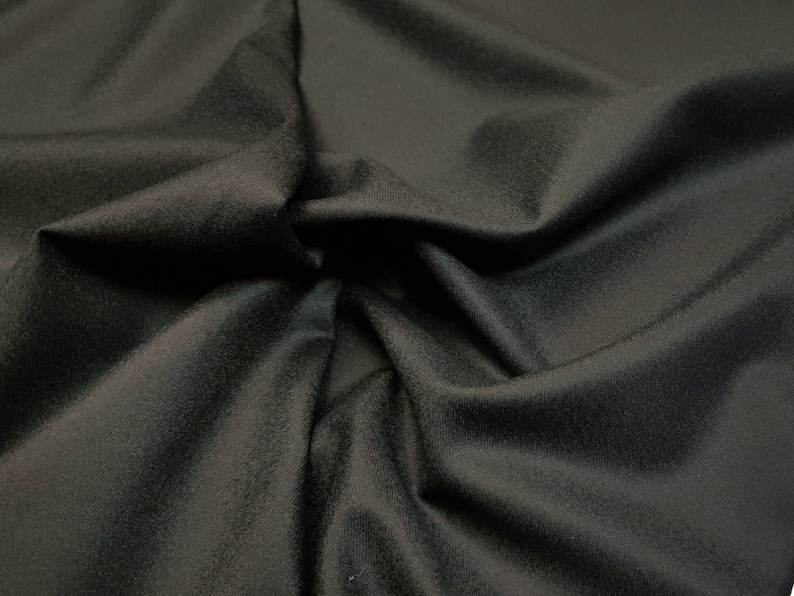 Puede incluir: Primer plano de una tela negra con una textura suave y lisa. La tela est&aacute; drapeada y doblada, mostrando su flexibilidad.