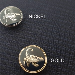May include: Two scorpion buttons, one nickel and one gold. The buttons are round and have a black background with a silver scorpion design.