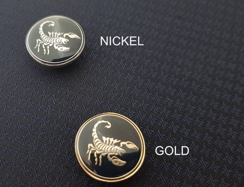 May include: Two scorpion buttons, one nickel and one gold. The buttons are round and have a black background with a silver scorpion design.