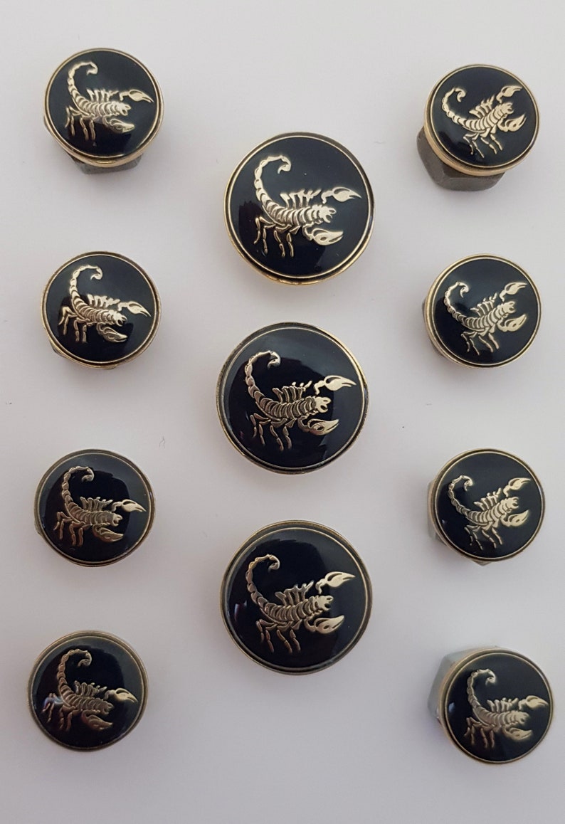 May include: Set of ten round, black and gold buttons featuring a scorpion design. The buttons are different sizes.
