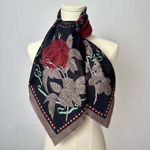 May include: A black silk scarf with a floral print of red roses, green leaves, and silver ribbons. The scarf has a brown border with a repeating pattern of small red dots.
