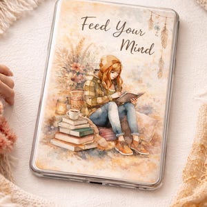 May include: Transparent phone case with a watercolour illustration and the text "Feed Your Mind." The image shows a person reading a book, with books, a coffee cup, and decorative elements. The colour scheme is warm, with autumnal tones.