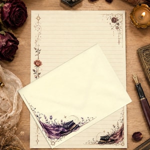 May include: A cream-coloured stationery sheet with horizontal lines and floral corner borders, partially covered by a matching envelope featuring a purple fabric and book illustration in the corner. The set includes a fountain pen and ink.