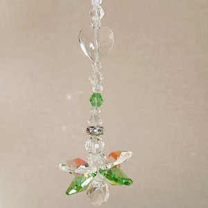May include: A hanging suncatcher ornament featuring a vertical strand of clear and lime green faceted crystal beads. The design includes a clear heart-shaped bead, a silver-toned metal spacer ring, and a bottom cluster of crystal flower petals.