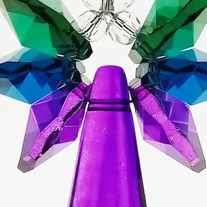 May include: A decorative crystal angel ornament with a purple body, blue and green wings, and clear crystal accents. The angel has a faceted design and is suspended against a white background.