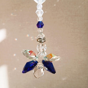 Op de afbeelding: Een hangend ornament met een heldere hartvormige kristal aan de bovenkant, gevolgd door een reeks heldere en diepblauwe gefacetteerde kristalkralen, een zilverkleurige tussenring en een centraal cluster van heldere en donkerblauwe kristalvormen.