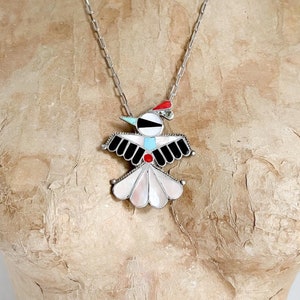 May include: A silver necklace featuring a multi-coloured bird pendant. The bird is crafted from a variety of stones, including turquoise, red coral, and black onyx. The pendant is attached to a silver chain.