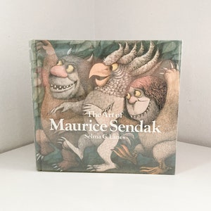 May include: A hardcover book titled "The Art of Maurice Sendak" featuring illustrations of whimsical creatures. The cover art showcases three monsters in shades of brown, gray, and pink, with the title and author's name in white text.