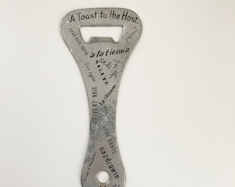 May include: A silver bottle opener with the text "A Toast to the Host" and "Good Luck!"  The opener also has the text "cead mile failte", "iss igia", "VIVA LA SALUTE", "nazdrowie", "Salud Y Pesetas", "SKALA", "SALUTE", "Wachiam", "CUNOTRE SANTE", and "alatienna".