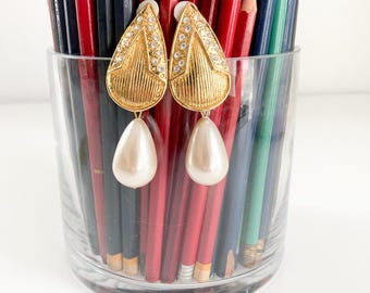 May include: A pair of gold tone dangle earrings with clear rhinestones and a white pearl drop.