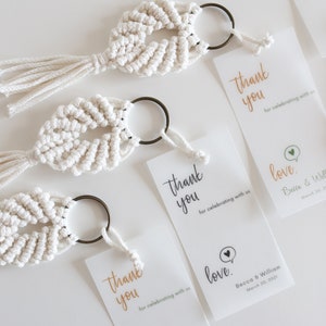 May include: Three white macrame keychains with a small metal ring and a tassel. Each keychain has a matching thank you card with the text "Thank you for celebrating with us" and "love" with the couple's names and wedding date.