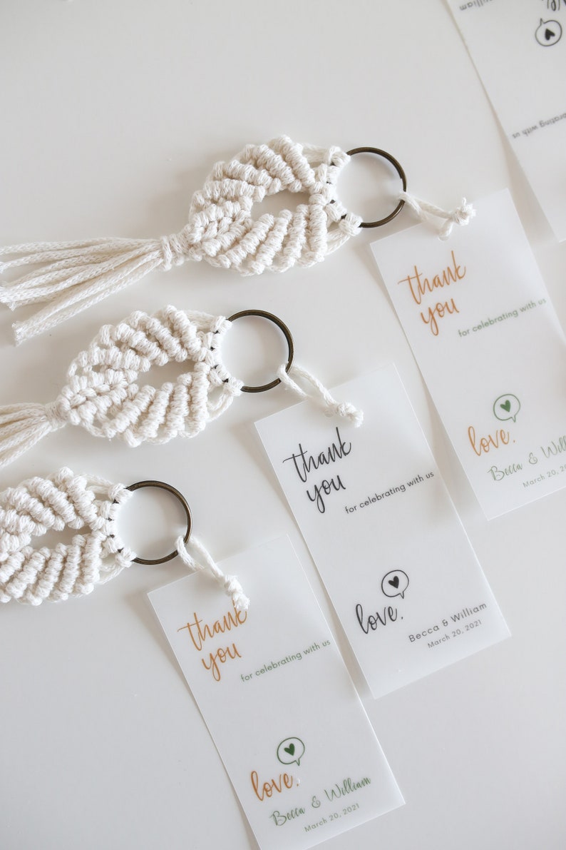 May include: Three white macrame keychains with a small metal ring and a tassel. Each keychain has a matching thank you card with the text "Thank you for celebrating with us" and "love" with the couple's names and wedding date.