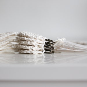 May include: A stack of white crocheted circles with tassels, attached to metal rings.