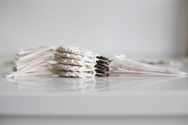 May include: A stack of white crocheted circles with tassels, attached to metal rings.