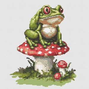 Op de afbeelding: Een groene kikker met rode ogen zit op een rode paddenstoel met witte stippen. De kikker is omringd door groen gras en kleinere paddenstoelen, wat een grillige, op de natuur geïnspireerde illustratie creëert.