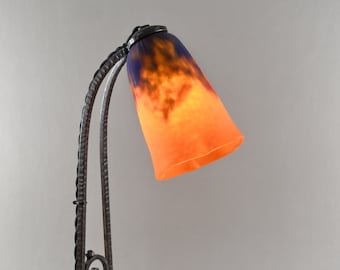 May include: A black wrought iron table lamp with a curved arm and a round base. The lampshade is made of glass with a mottled orange and purple design.