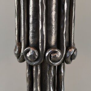 May include: Close-up of a silver metal candlestick with a decorative, twisted design. The base of the candlestick has a series of small, curled loops.