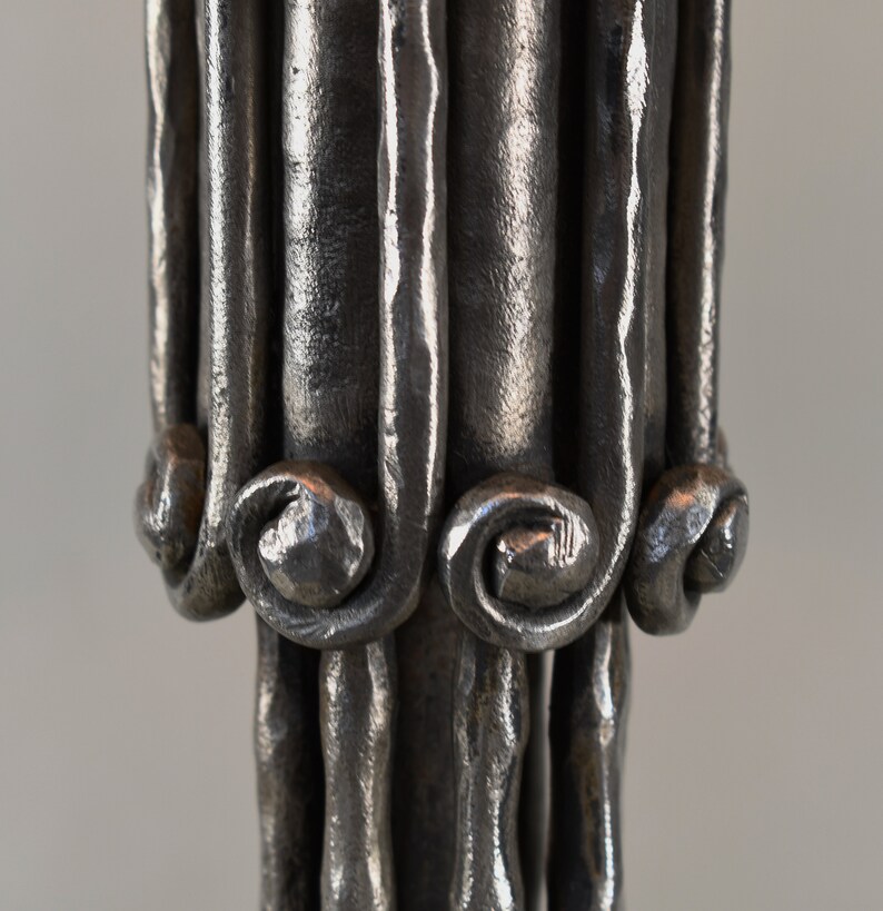 May include: Close-up of a silver metal candlestick with a decorative, twisted design. The base of the candlestick has a series of small, curled loops.