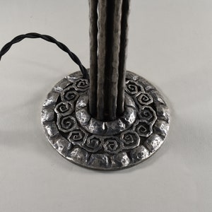 May include: A silver metal table lamp base with a textured, hammered finish. The base features a circular design with a repeating pattern of spirals.