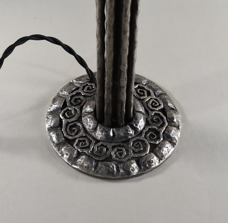 May include: A silver metal table lamp base with a textured, hammered finish. The base features a circular design with a repeating pattern of spirals.