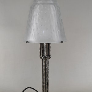 May include: A silver table lamp with a frosted glass shade. The shade has a textured, bubble-like design. The base of the lamp is made of metal and has a decorative design.