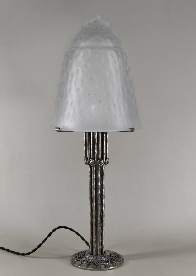 May include: A silver table lamp with a frosted glass shade. The shade has a textured, bubble-like design. The base of the lamp is made of metal and has a decorative design.