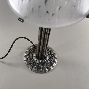 May include: A silver table lamp with a frosted glass shade and a base with a decorative design. The lamp has a black cord.