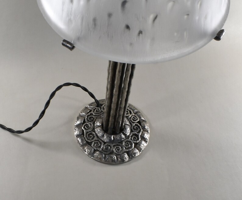 May include: A silver table lamp with a frosted glass shade and a base with a decorative design. The lamp has a black cord.