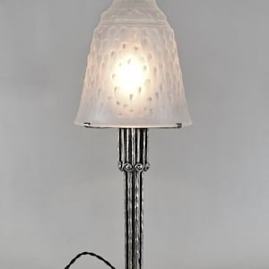 May include: A silver table lamp with a frosted glass shade. The shade has a textured, bumpy surface. The lamp base is made of metal and has a cylindrical shape with decorative details.